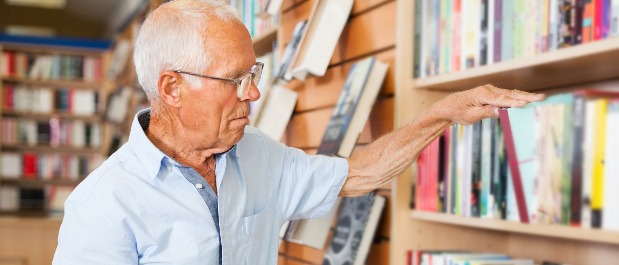 Auswahl im Bücherregal Senior greift nach einem Buch im oberen Regal einer Bibliothek