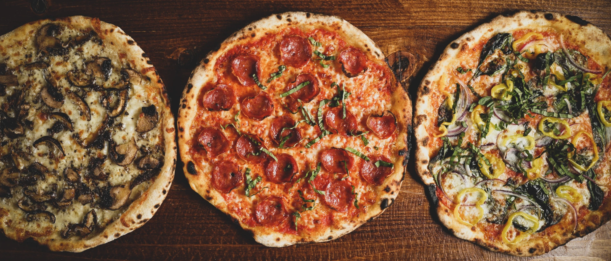 Drei verschiedene Pizzen nebeneinander Drei unterschiedliche Pizzen auf Holzbrett, Symbol für Pizza-Franchises