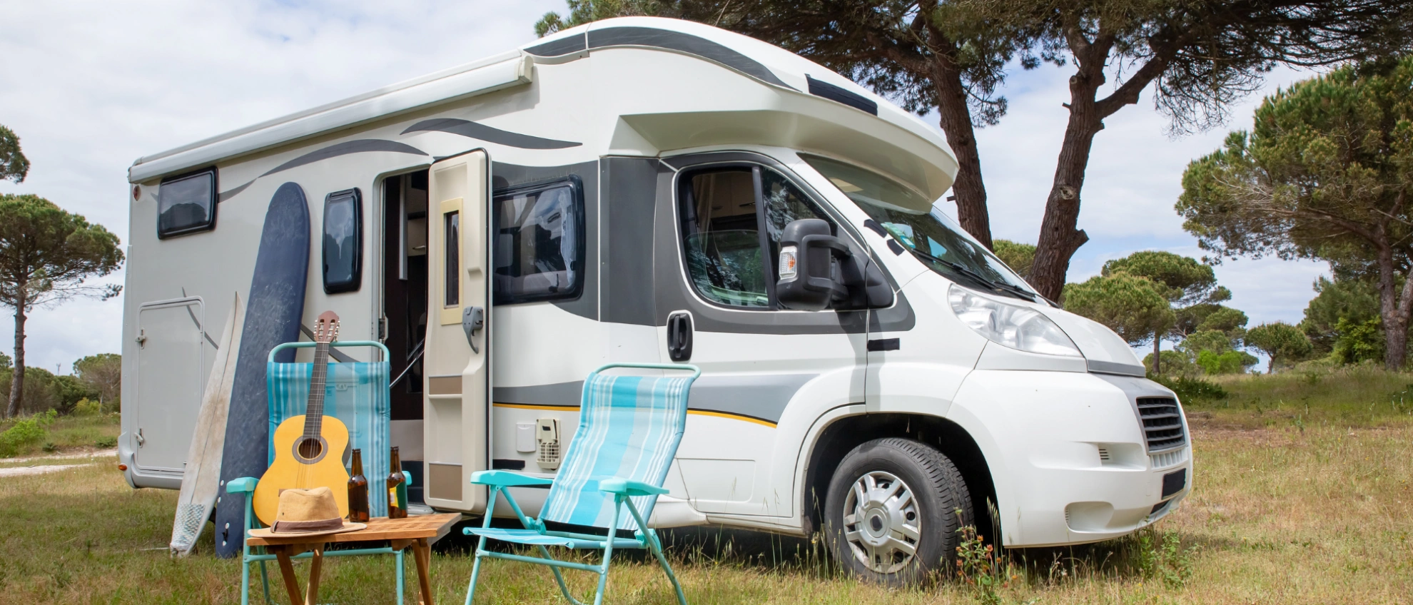 Entspanntes Camping Wohnmobil mit Campingstühlen davor auf einer grünen Wiese unter Bäumen