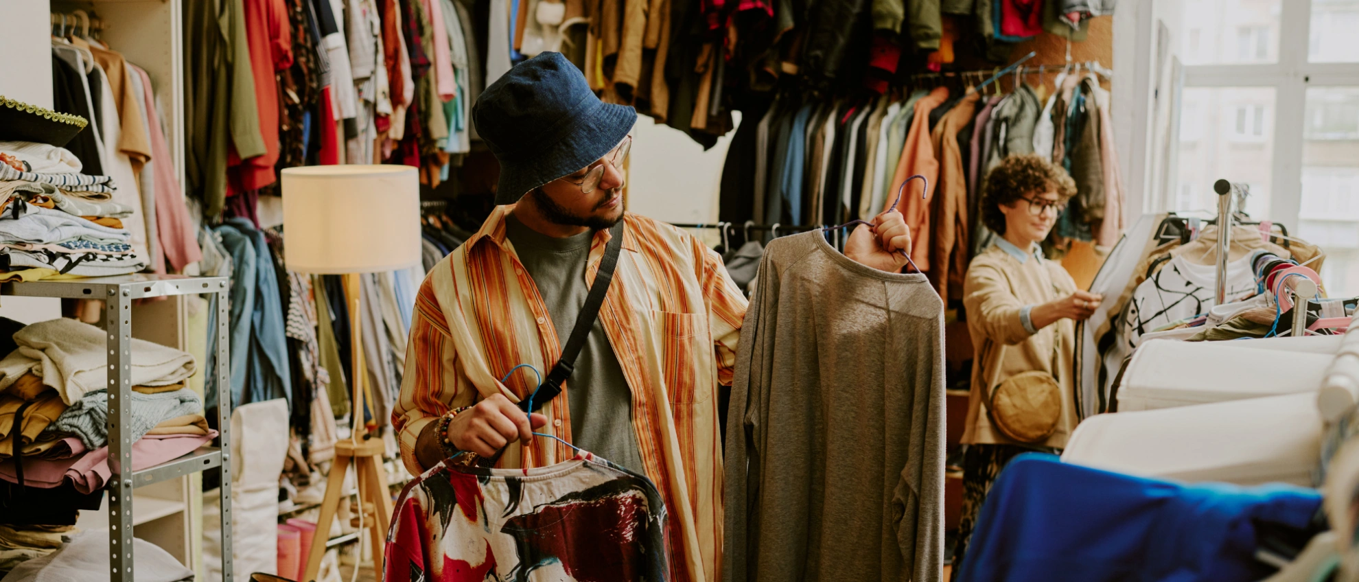 Stöbern im Second-Hand-Laden Frau durchstöbert Kleiderständer in einem hellen Second-Hand-Shop mit Vintage-Kleidern