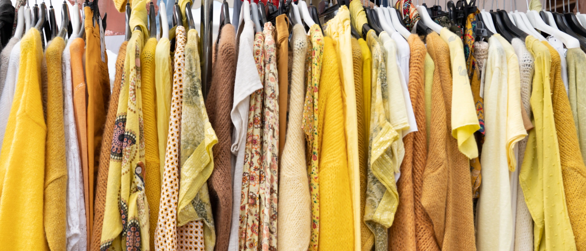 Farbenfrohe Kleiderstange Second-Hand-Kleiderstange mit gelb-beigen Kleidungsstücken in abgestimmten Farbtönen