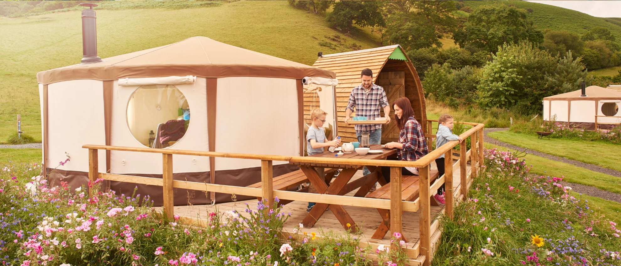 Komfortables Glamping mit Holzterrasse und Naturblick Gäste entspannen auf der Terrasse eines Rundzelts inmitten einer blühenden Wiese