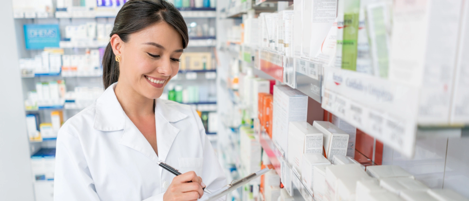 Junge Apothekerin in weißem Kittel sucht ein Medikament im Apothekenregal