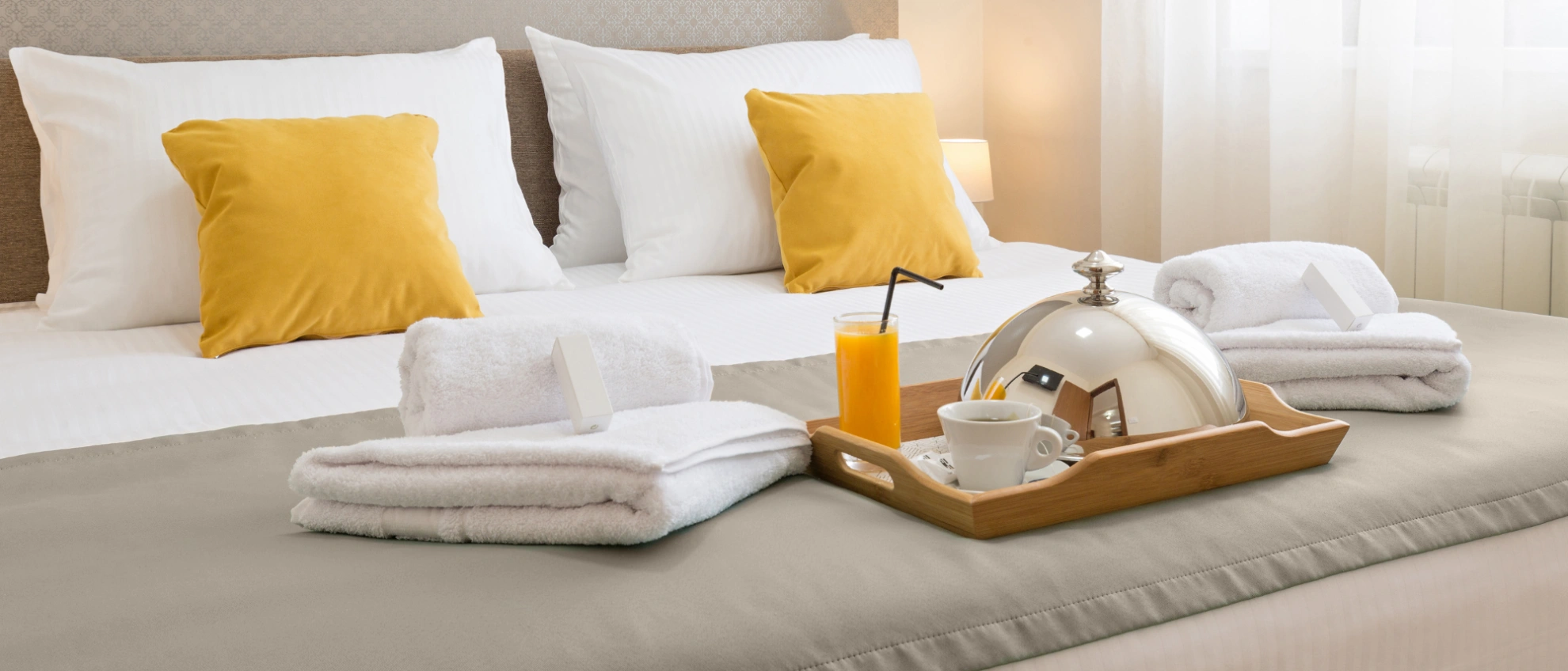 Modernes Doppelbett mit gelben Kissen, sauber gefaltetem Handtuchset und Frühstückstablett