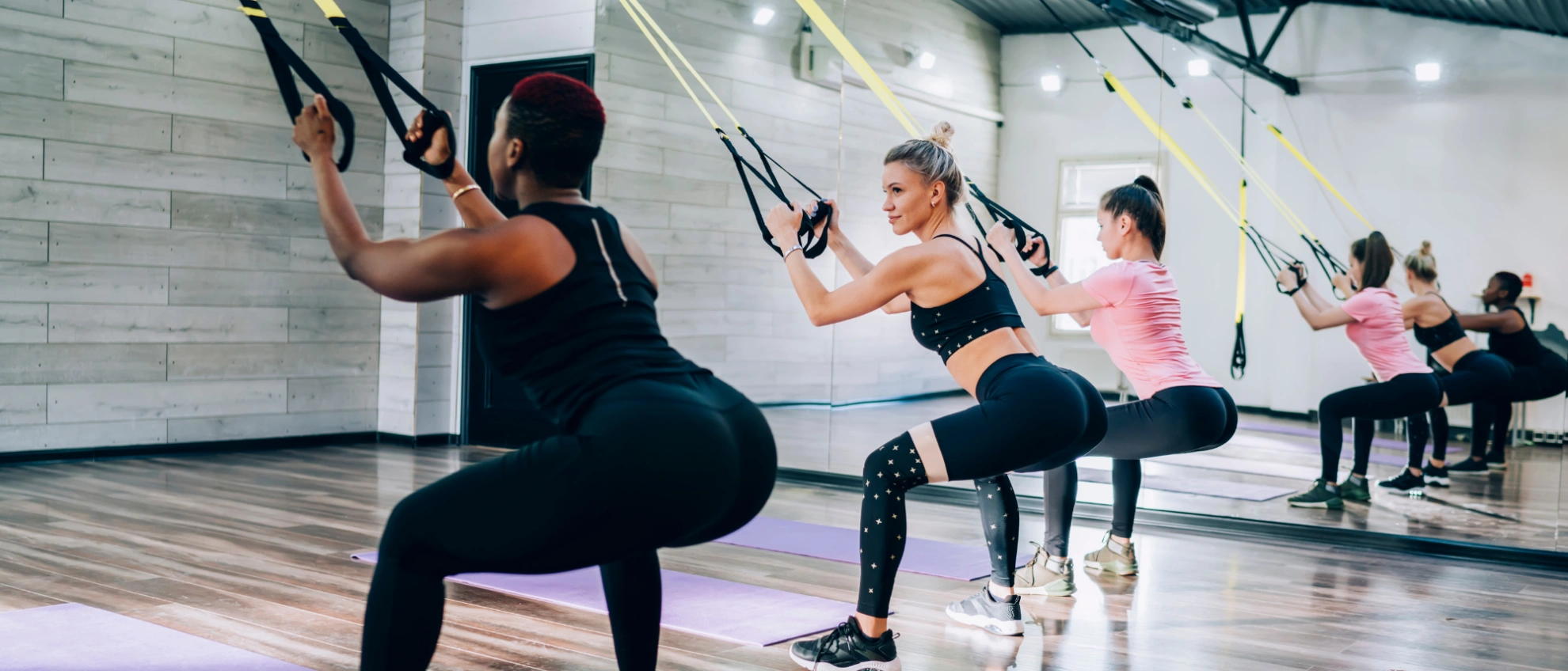 TRX-Training mit Trainerin Frauen trainieren mit TRX-Bändern in einem hellen Studio unter professioneller Anleitung