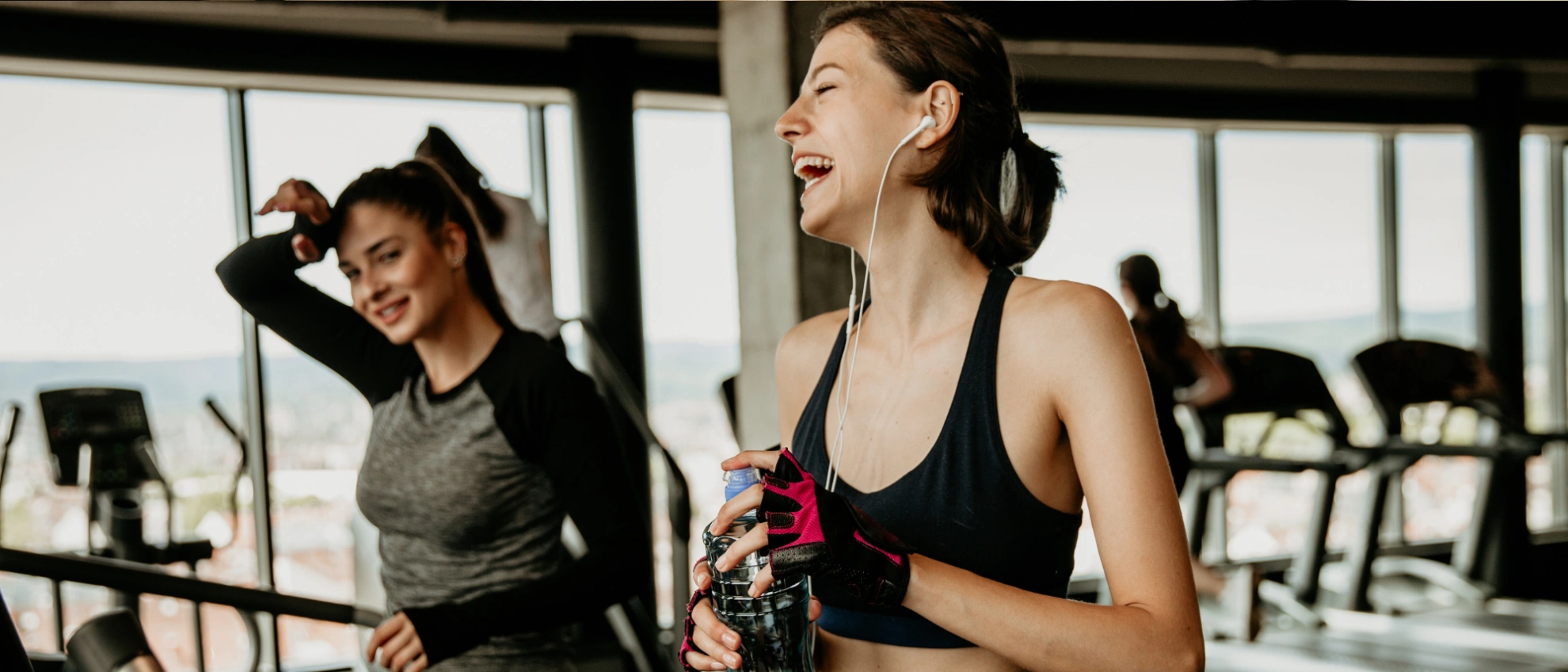 Freude nach dem Training Zwei Frauen in Sportkleidung lachen nach dem Training im Fitnessraum und trinken Wasser