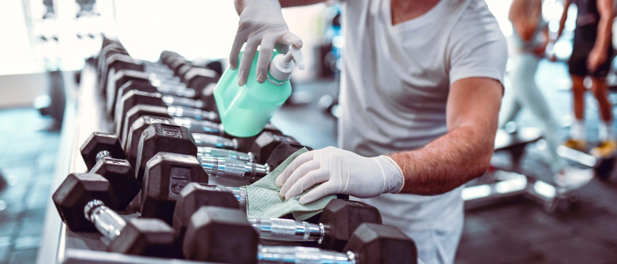 Desinfektion von Hanteln im Fitnessstudio Mann in Sportkleidung reinigt Hanteln im Studio mit Desinfektionsmittel nach dem Training