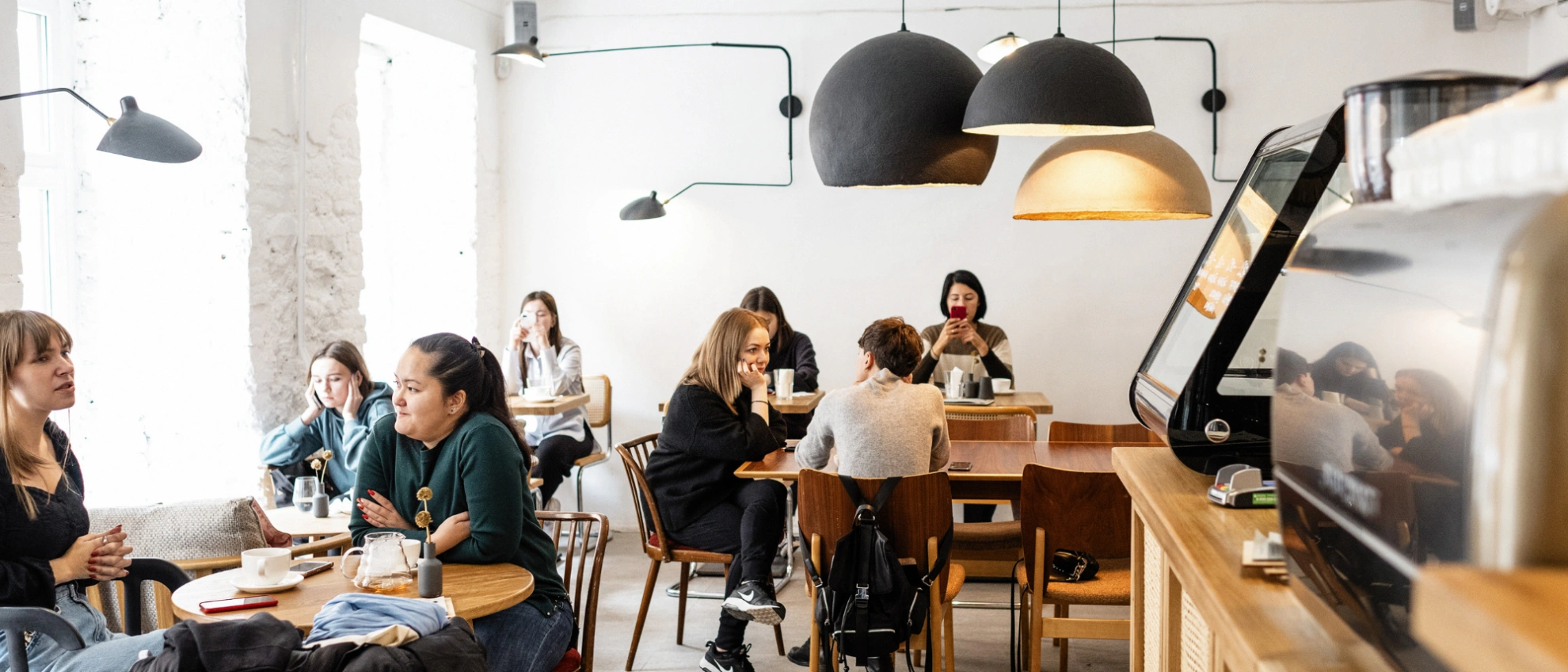 Helles, stilvoll eingerichtetes Café mit mehreren Gästen beim Arbeiten oder Entspannen
