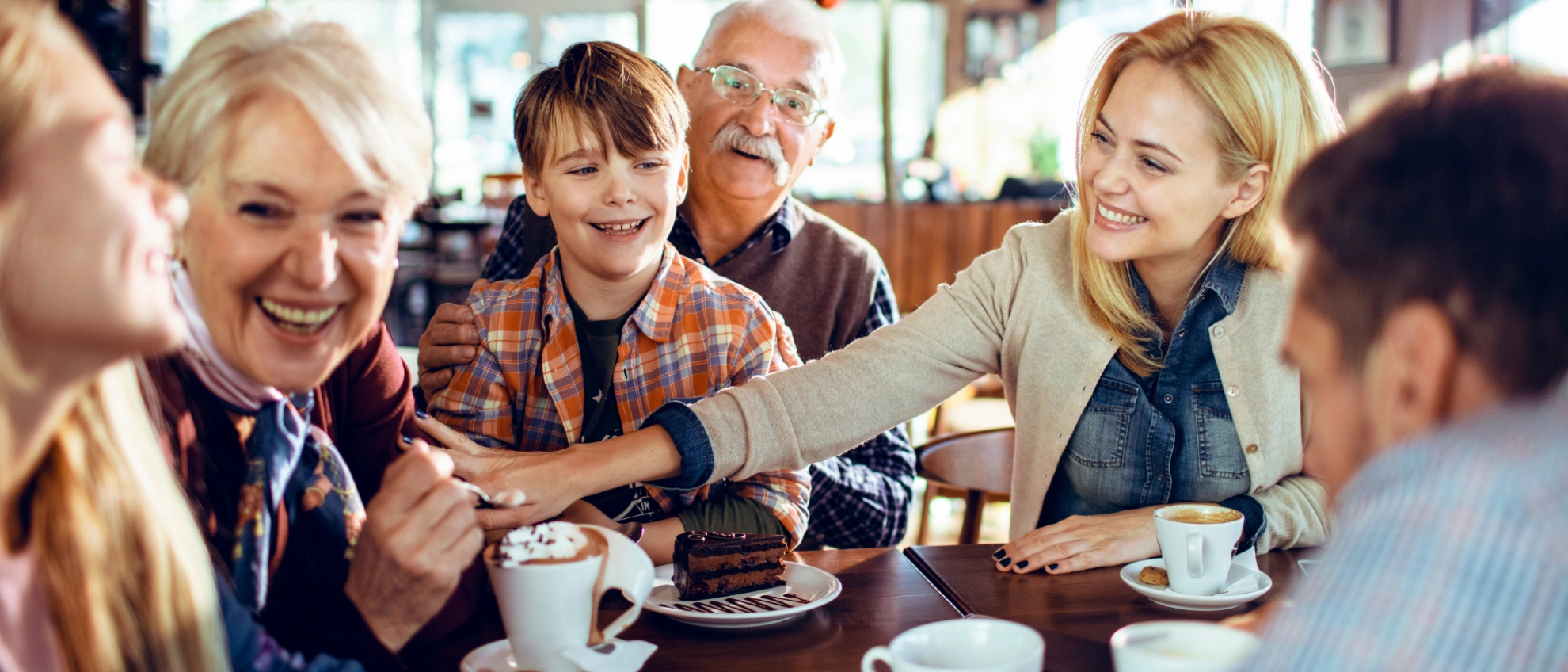 Gruppe älterer und jüngerer Menschen lacht gemeinsam bei Kaffee und Kuchen im Café