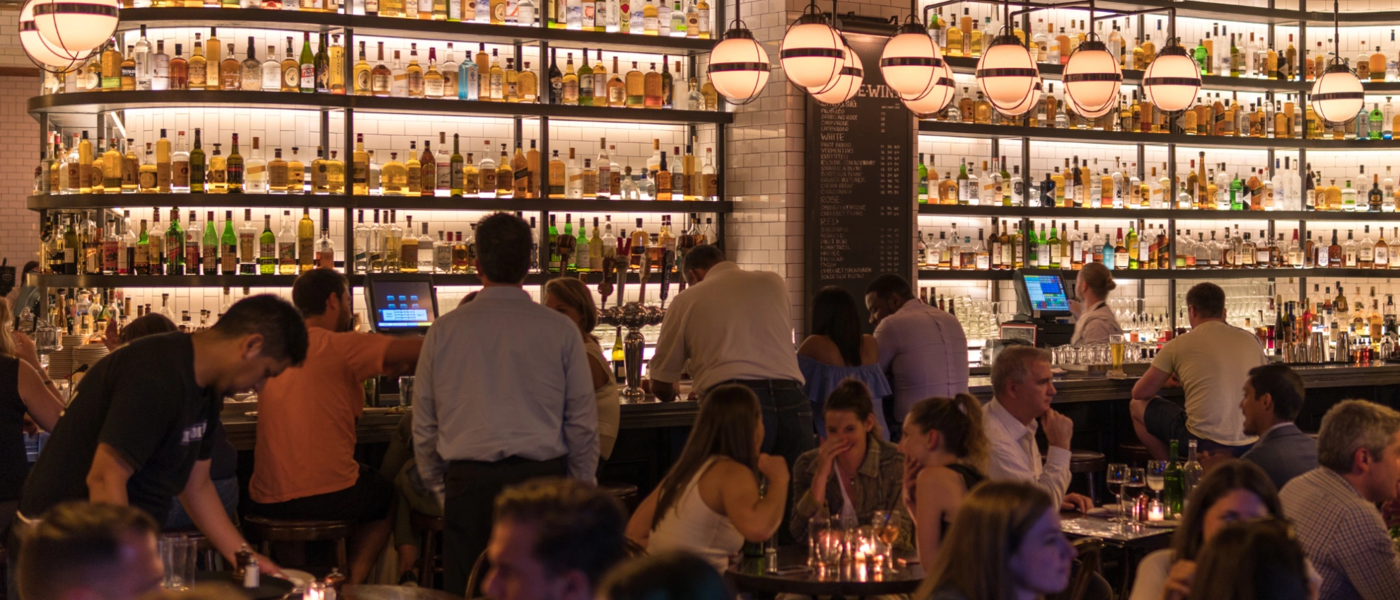 Edle Bar mit hoher Flaschenwand, gedämpftem Licht und Gästen im Vordergrund