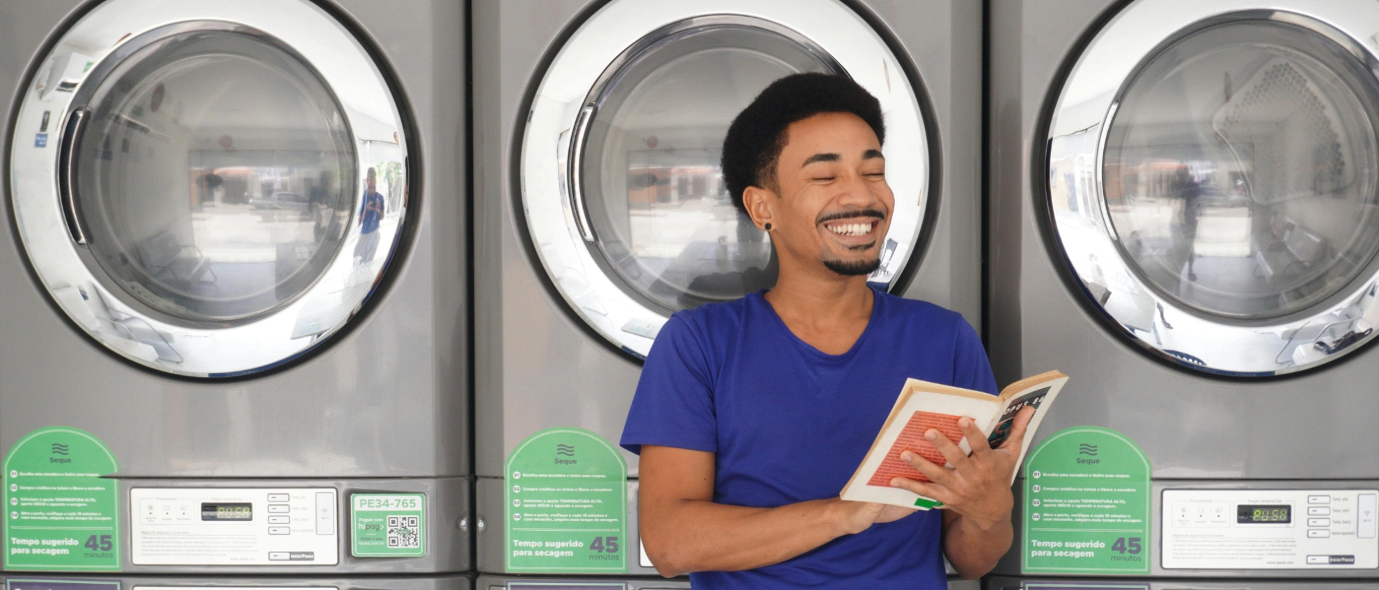 Mann liest ein Buch vor großen Waschmaschinen in einem modernen Waschsalon