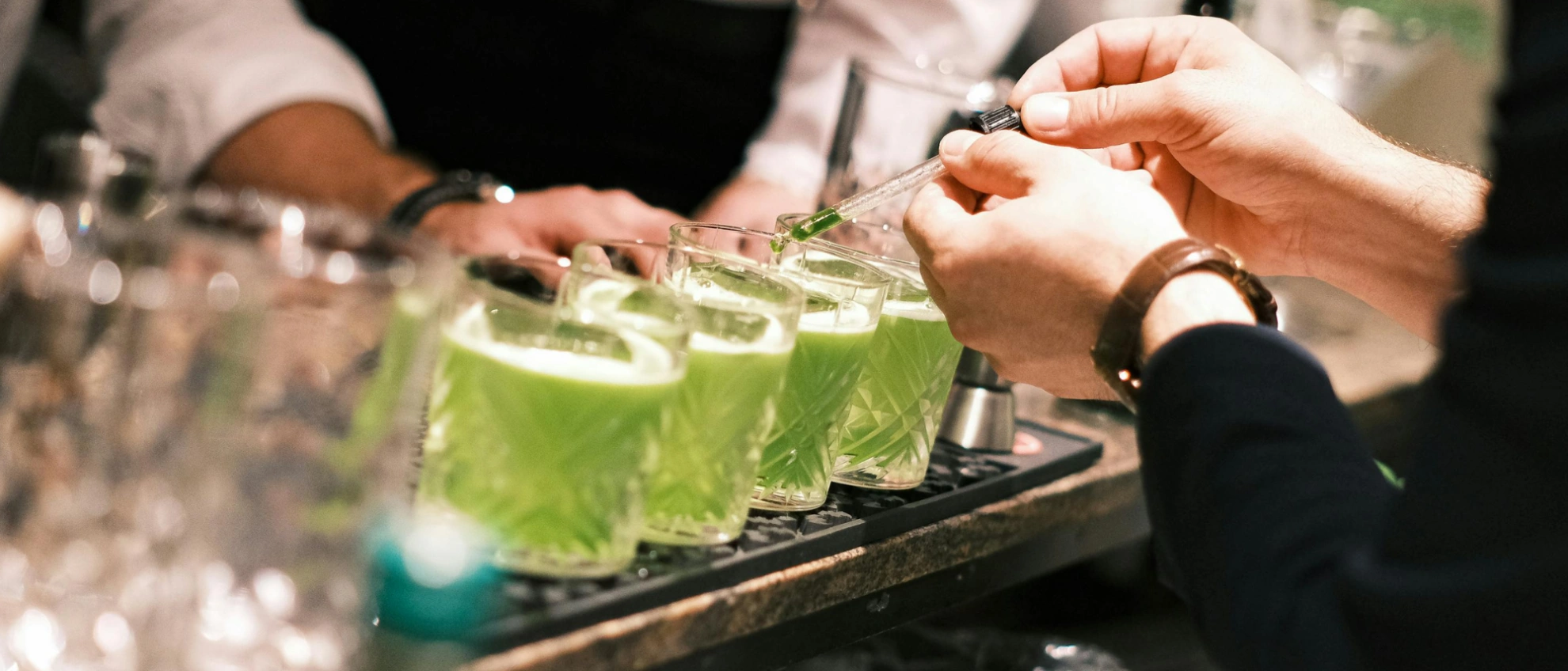 Hände eines Barkeepers richten mehrere leuchtend grüne Cocktails gleichzeitig an