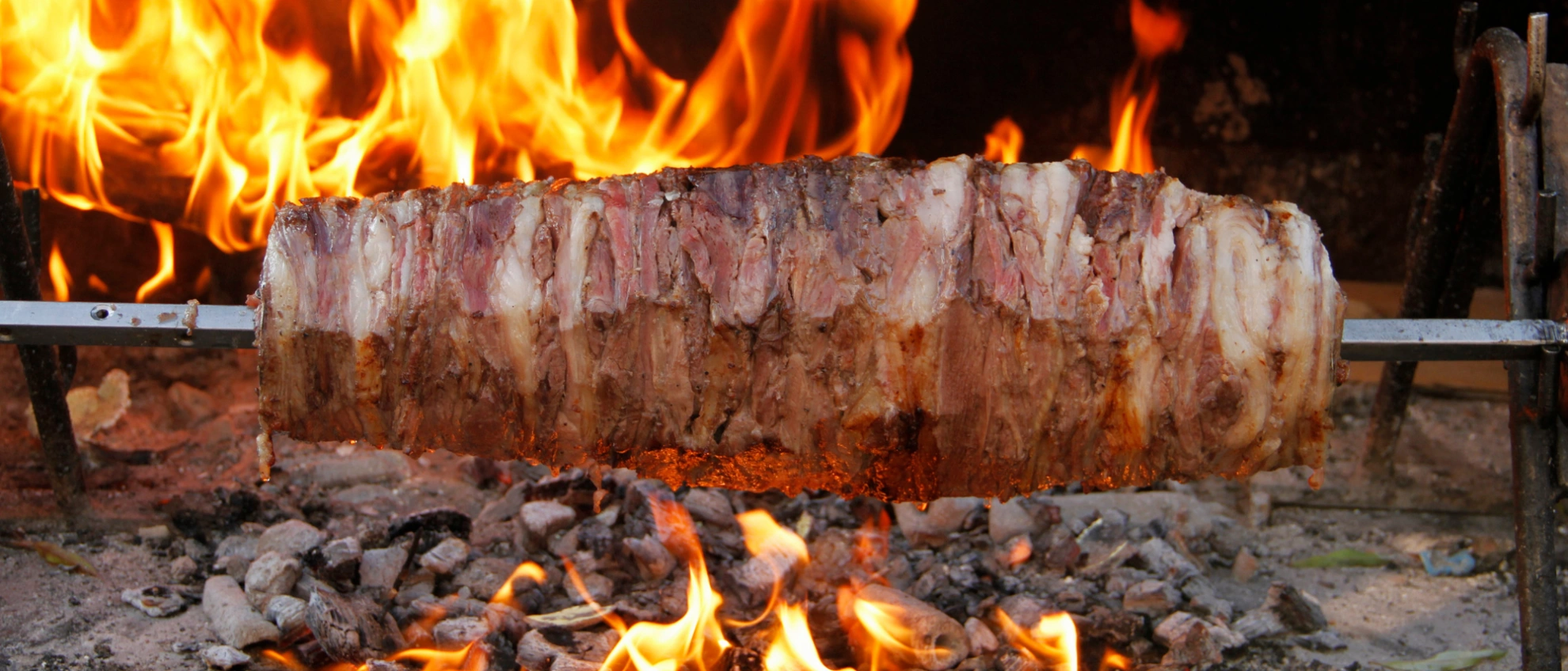 Großes Stück Fleisch wird horizontal über offenen Flammen gegart