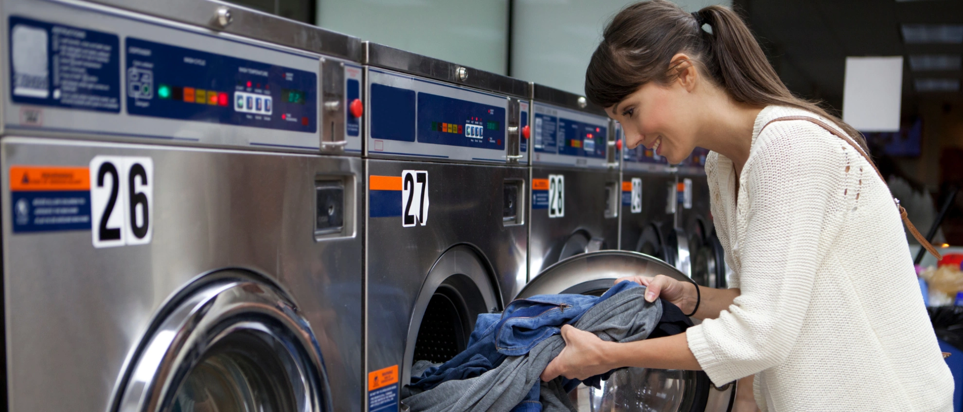  Frau belädt eine Industriewaschmaschine in einem modernen Waschsalon