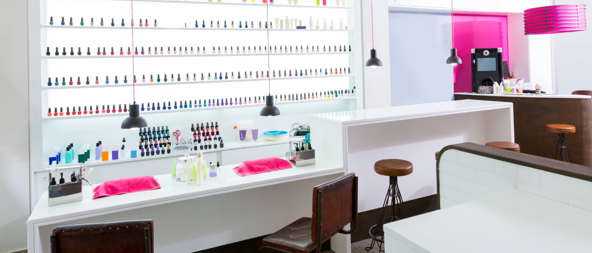 Innenraum eines hellen Studios mit Wand voller Nagellackflaschen und Maniküretischen