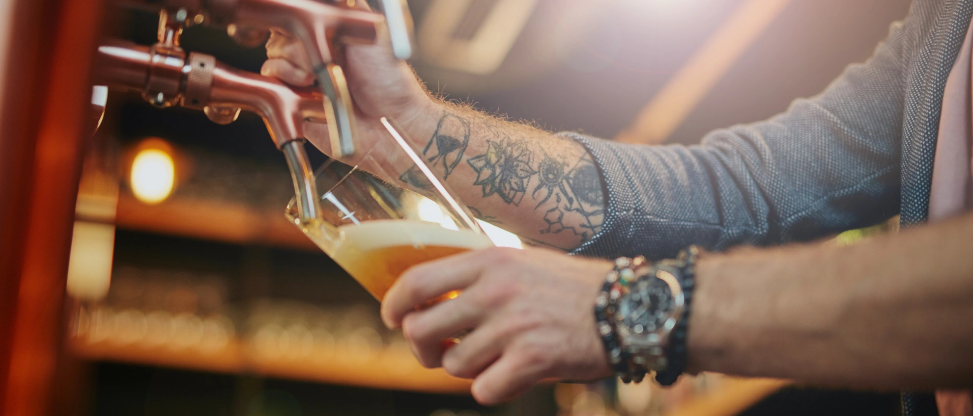 Zapfen mit Stil Barkeeper mit Tattoos schenkt frisch gezapftes Bier in ein Glas ein