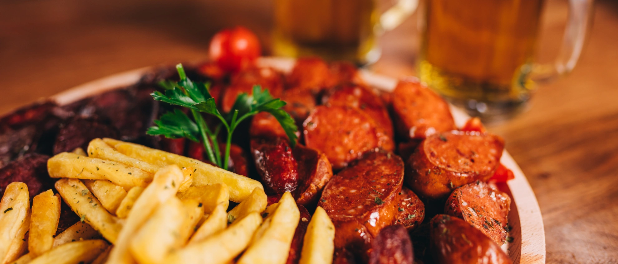 Deftiges Essen zur Maß Bier Traditioneller Bierteller mit Bratwurst, Sauerkraut und Gemüse, daneben ein Glas Bier