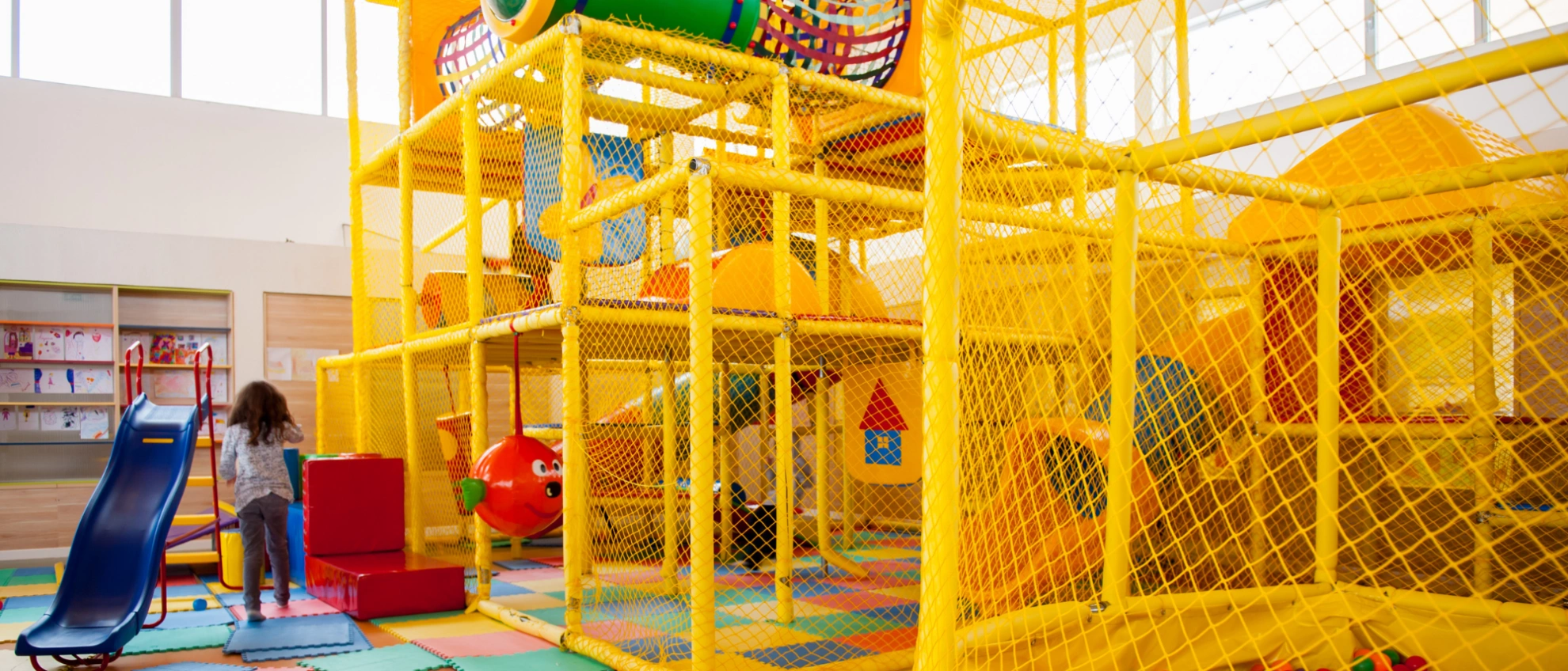 Leere Indoor-Spielanlage mit gelbem Gitter, Rutschen und Kletterbereich