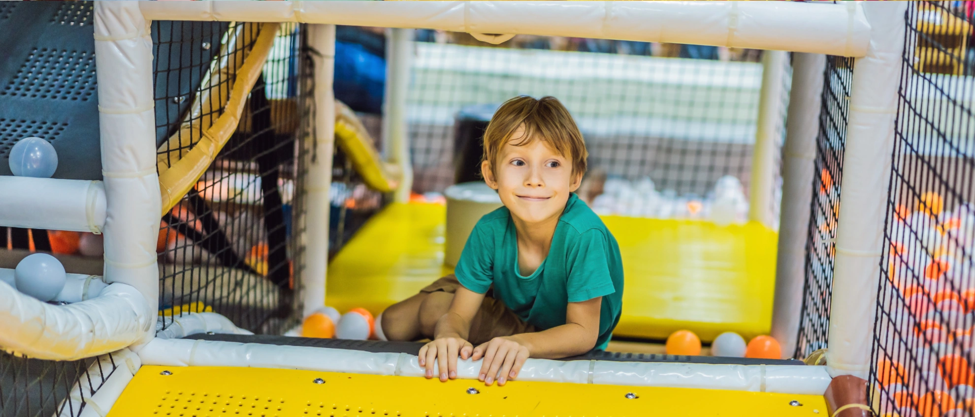 Junge sitzt entspannt in einem bunten Kletterbereich mit Netzen und Rutschen