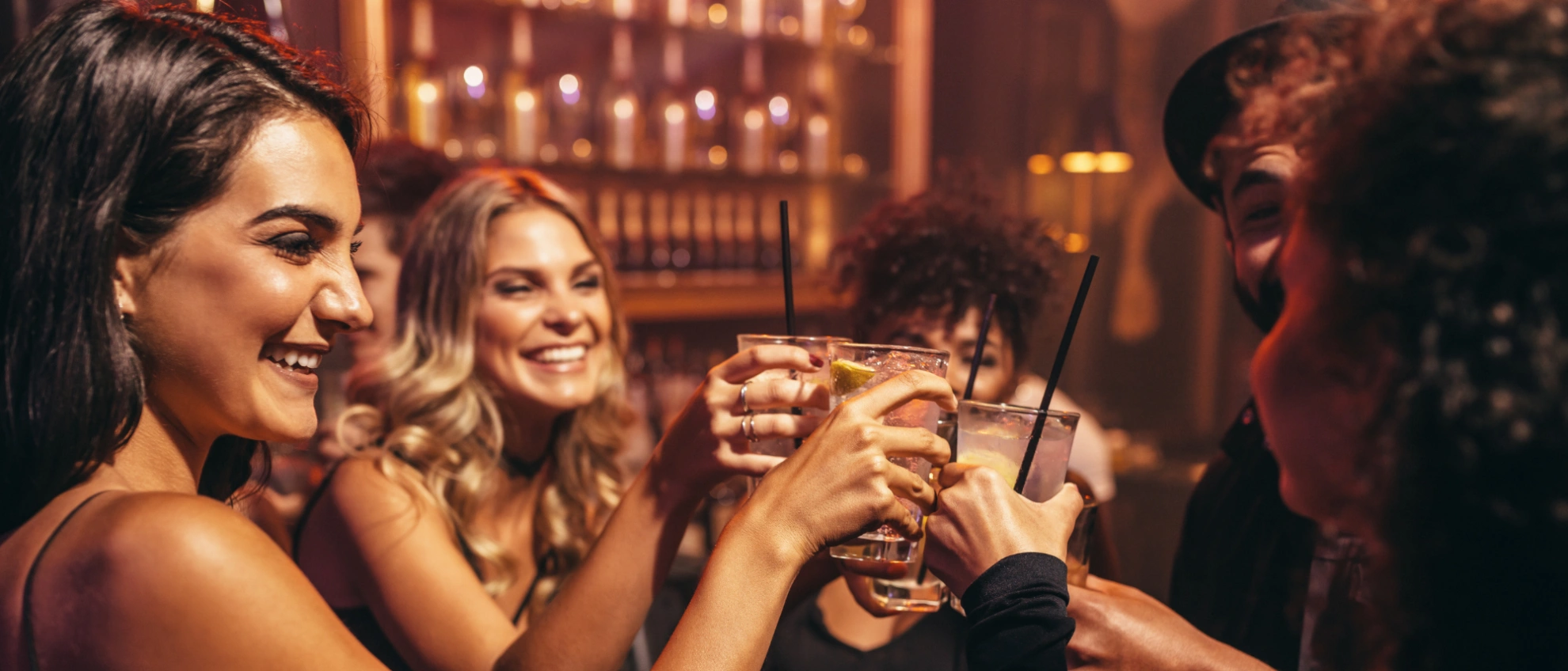 Gruppe junger Leute prostet sich in gemütlicher Bar-Atmosphäre zu