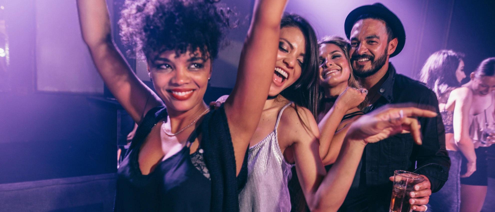 Gruppe feiernder Personen tanzt und lacht in einer bunt beleuchteten Disco