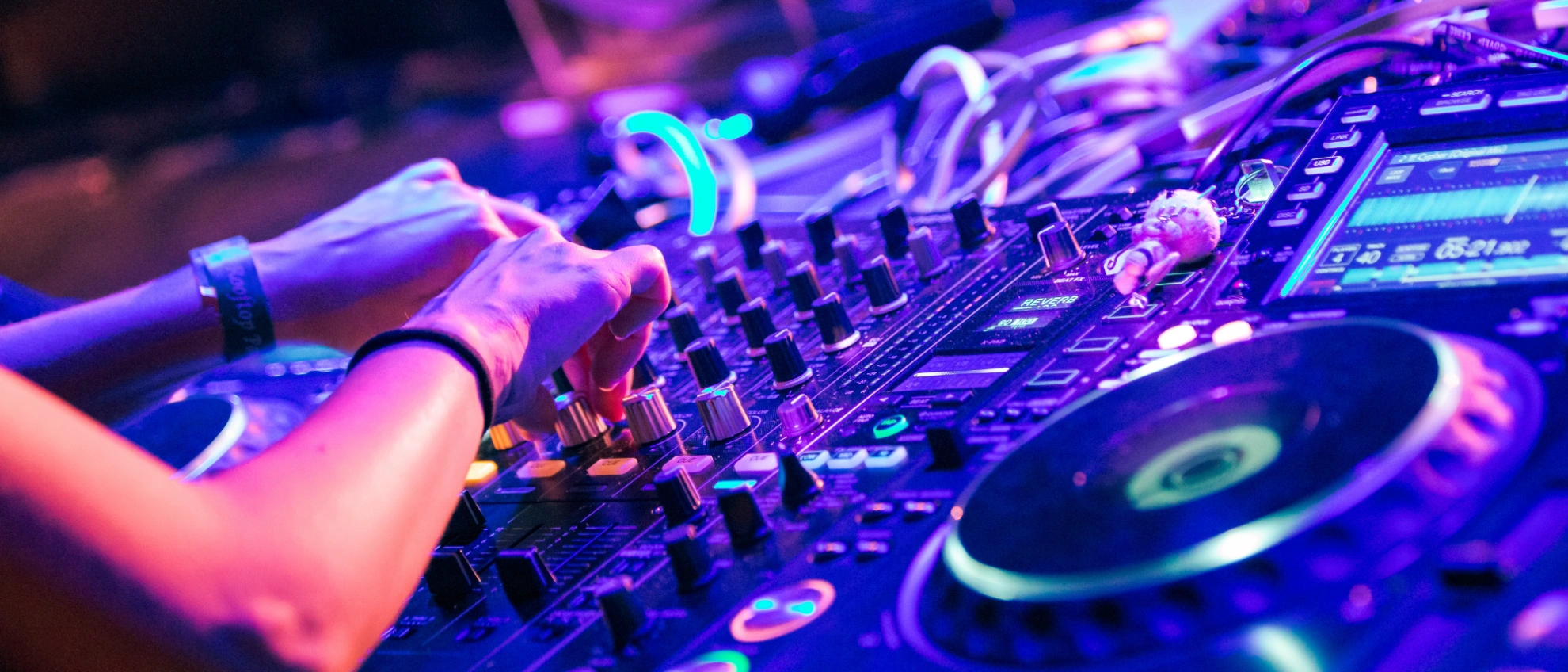 Hände von Partybesuchern und DJ auf einem beleuchteten Mischpult mit Turntables