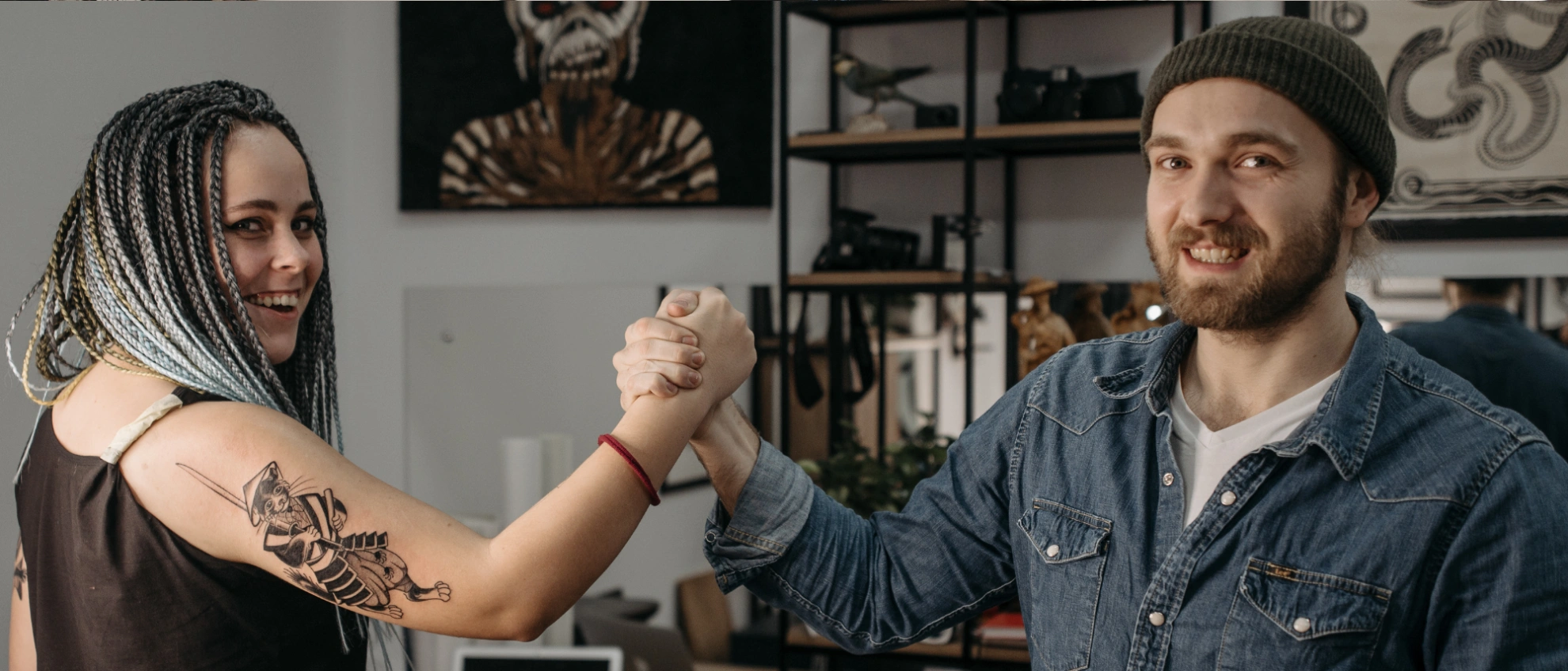 Stolz auf das Ergebnis – Kundin zeigt ihr neues Tattoo Tätowierer und Kundin mit frisch tätowiertem Oberarm geben sich die Hand im Studio