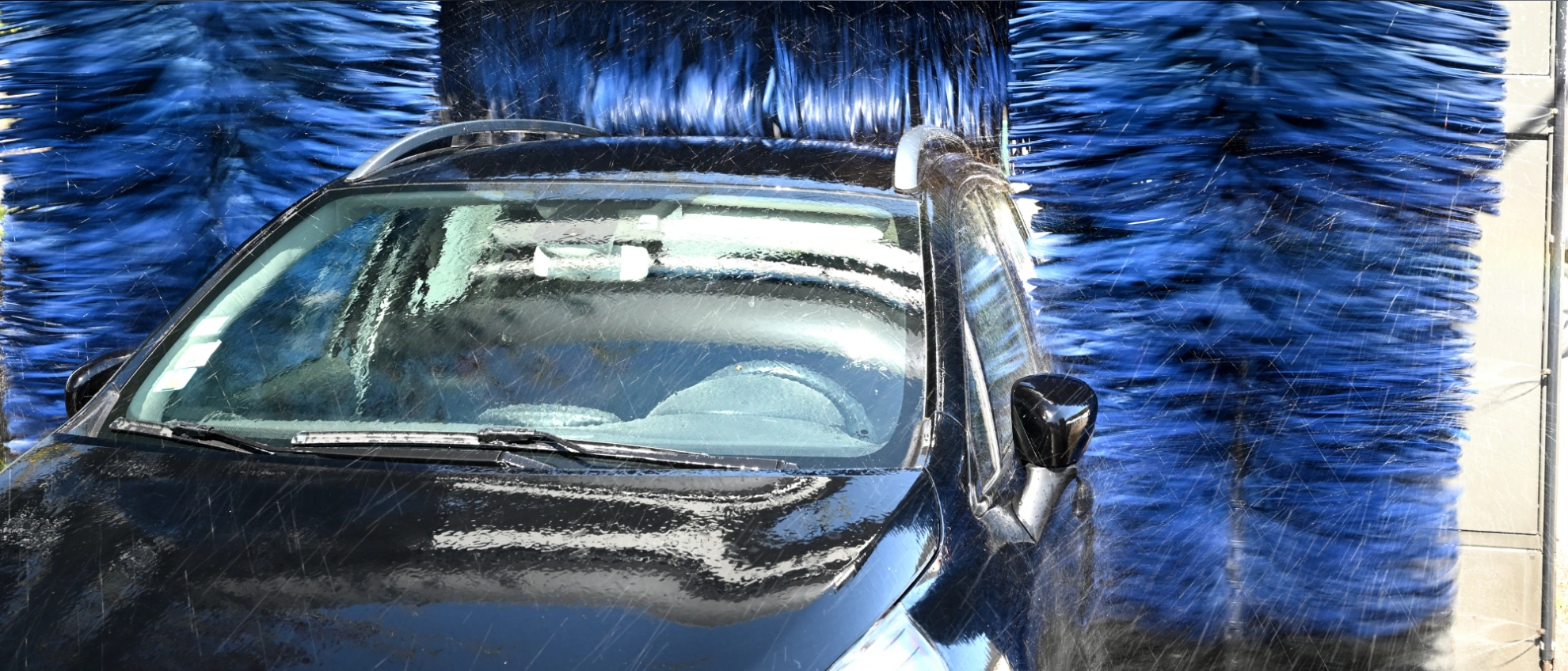 Fahrzeugwäsche in moderner Portalwaschanlage Auto durchfährt eine automatische Waschstraße mit blauen Bürsten