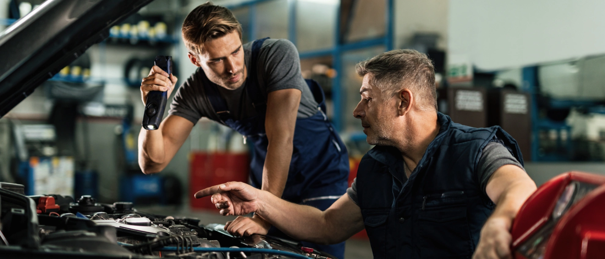 Zwei Männer unterhalten sich lachend in einer modernen Autowerkstatt, einer sitzt im Auto