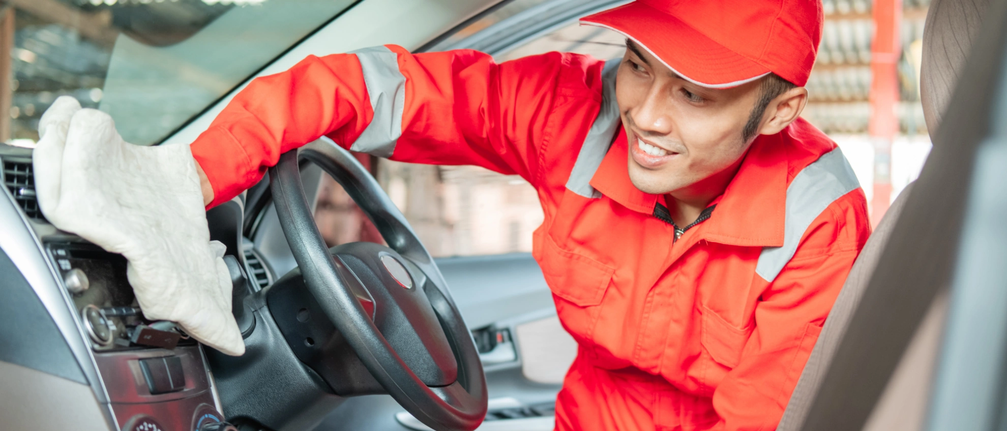 Fahrzeugaufbereitung mit Fokus auf den Innenraum Mitarbeiter in roter Arbeitskleidung reinigt das Armaturenbrett eines Autos