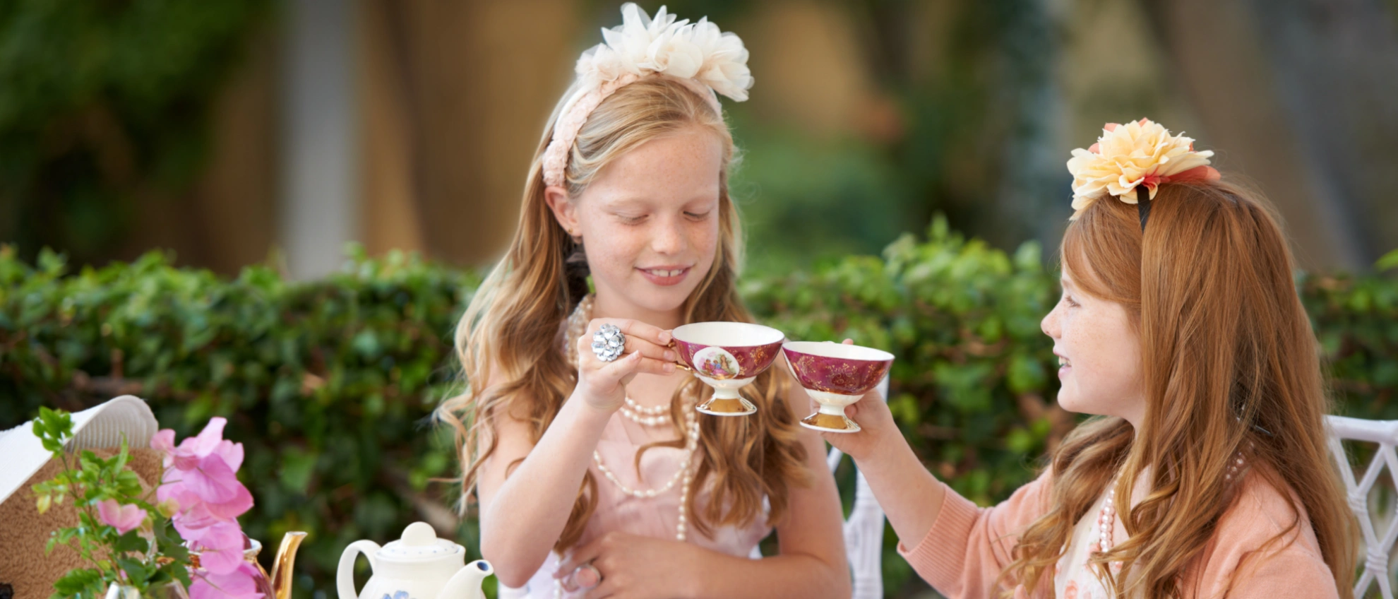 Zwei Mädchen mit Kronen stoßen mit kleinen Teetassen bei einer Gartenparty an
