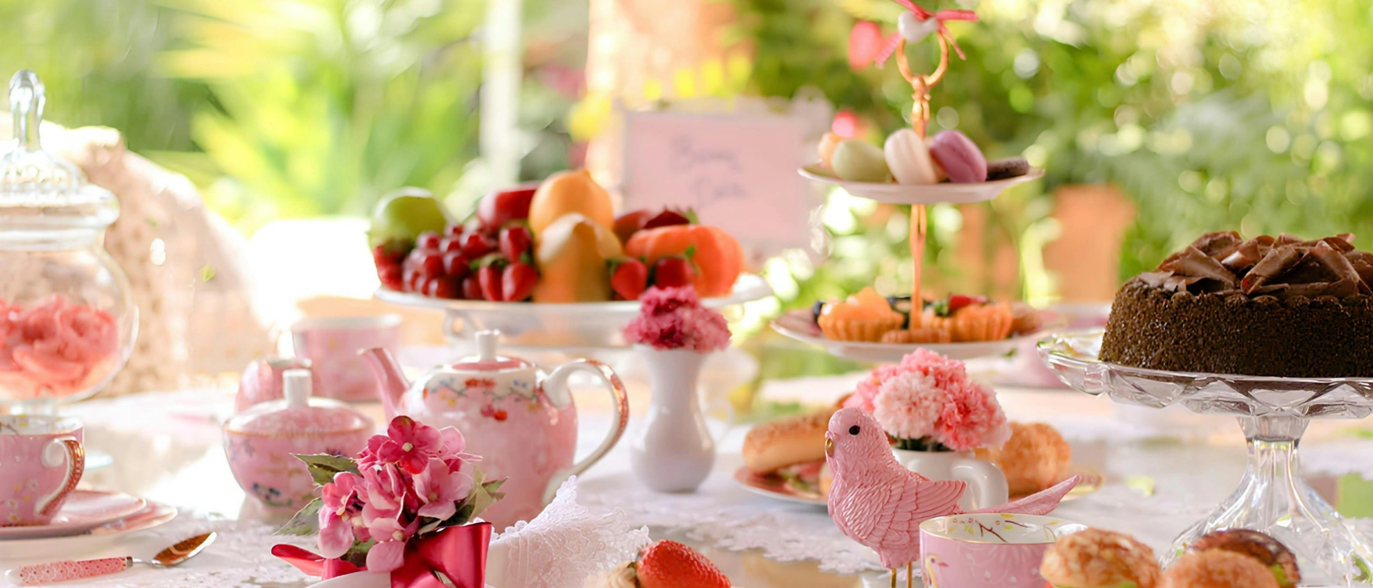 Kindgerecht dekorierter Tisch mit Tee, Kuchen und frischem Obst bei einer Feier im Freien