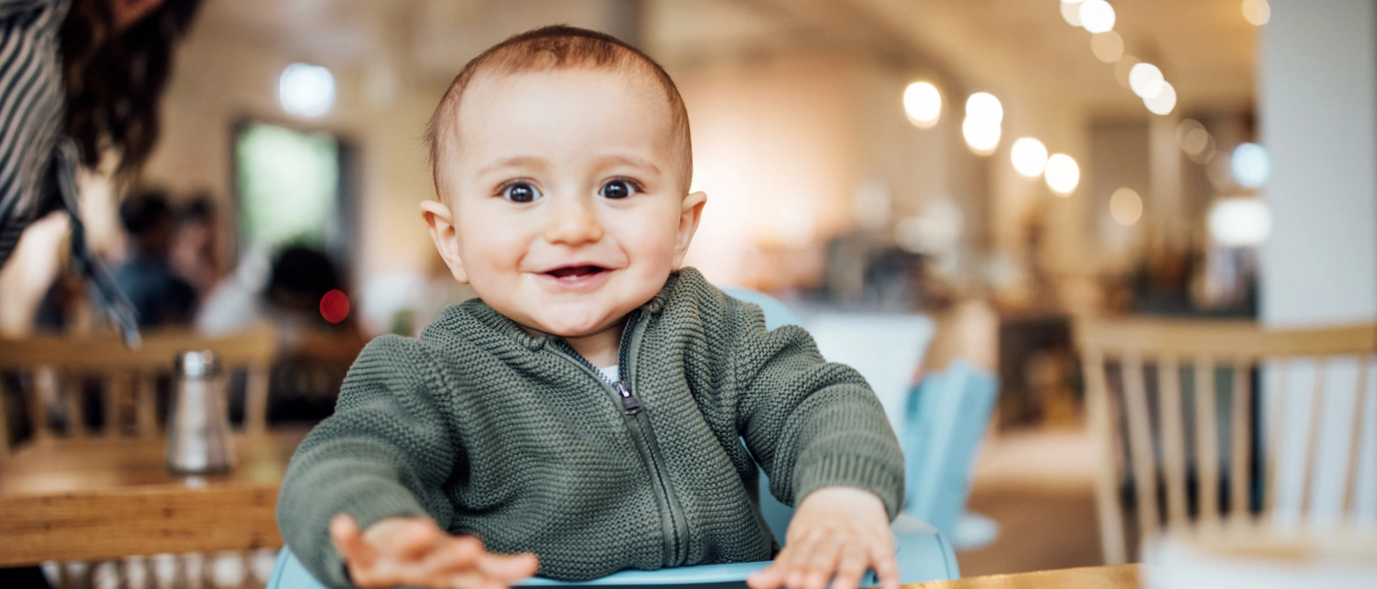 Fröhliches Baby sitzt am Tisch in einem hellen, familienfreundlichen Café