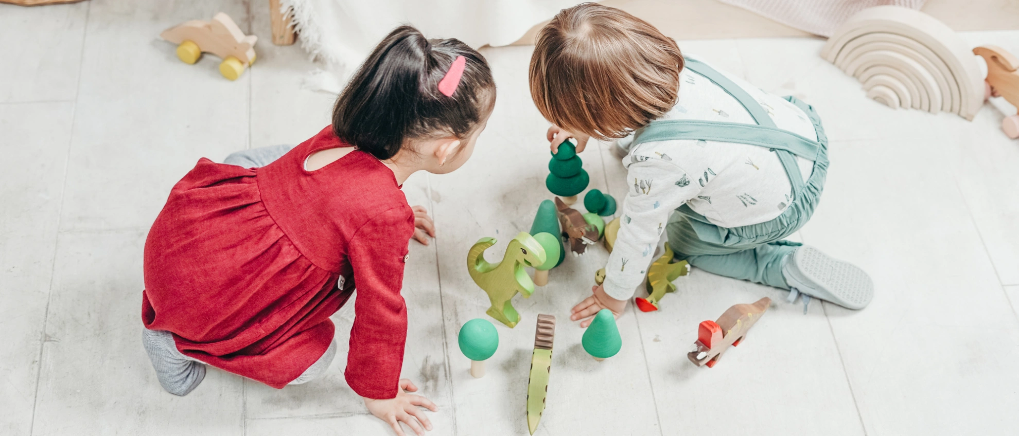 Zwei Kinder spielen mit Spielzeug auf dem Boden in einem hellen Raum mit Spielbereich