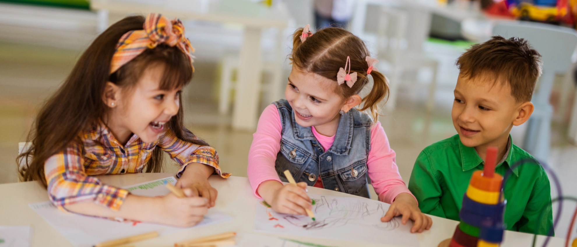 Drei Kinder malen mit bunten Farben am Tisch und lachen zusammen