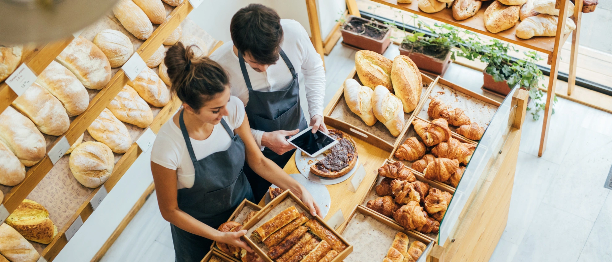 Frische Backwaren und freundlicher Service – Blick in eine moderne Bäckerei Bäckerei-Team bedient gemeinsam Kunden an einer Theke mit Brotwaren, Blick von oben auf den Verkaufsbereich