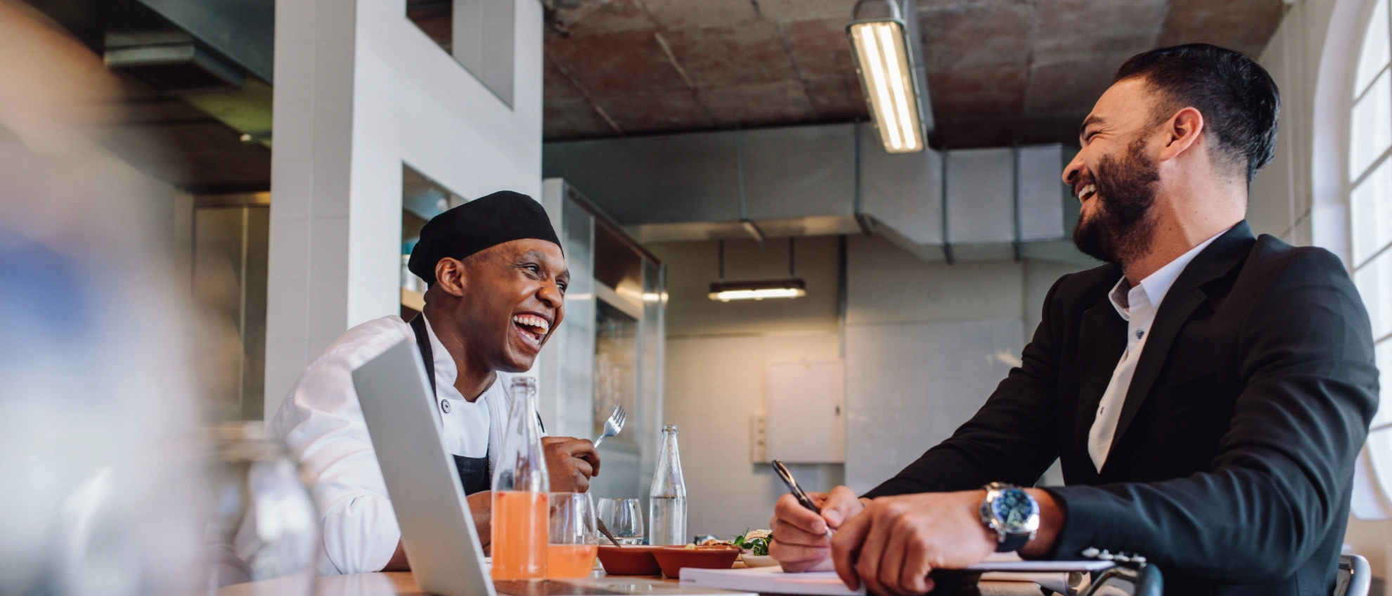Geschäftliches Gespräch im Restaurant zwischen Koch und Manager Zwei Männer, einer im Anzug und einer im Kochoutfit, unterhalten sich an einem Tisch im Restaurant