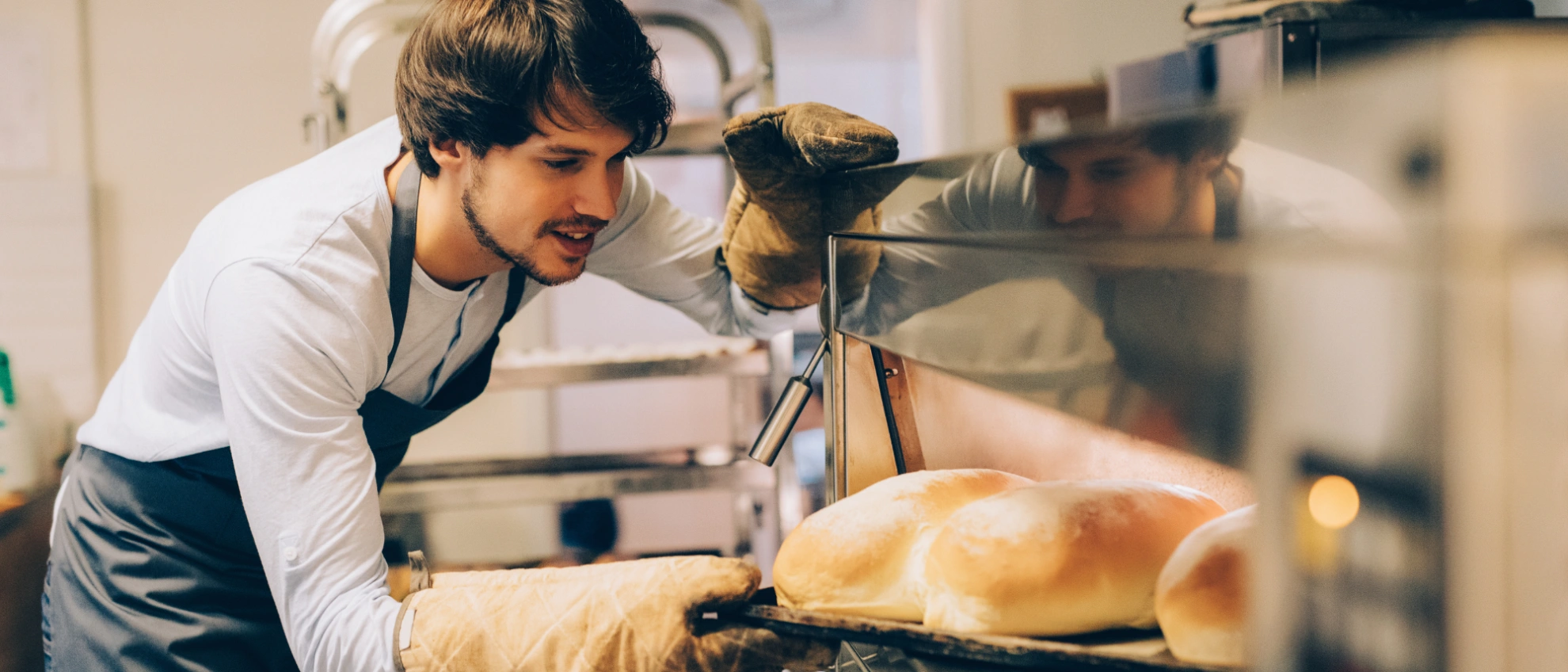 Bäcker holt ofenfrisches Brot aus der Backstube Bäcker holt frische Brote mit Ofenhandschuhen aus dem Ofen in einer Backstube