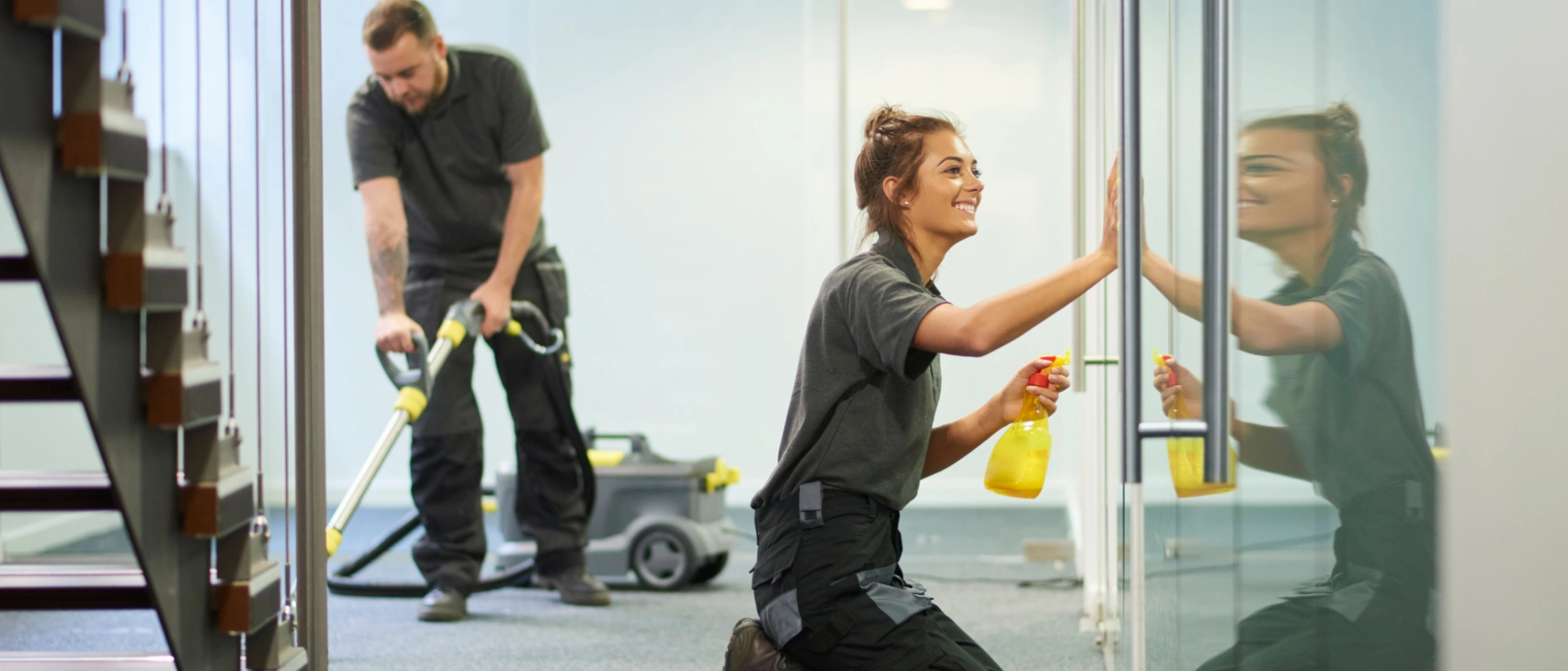 Zwei Reinigungskräfte putzen Glasflächen im Eingangsbereich eines Bürokomplexes
