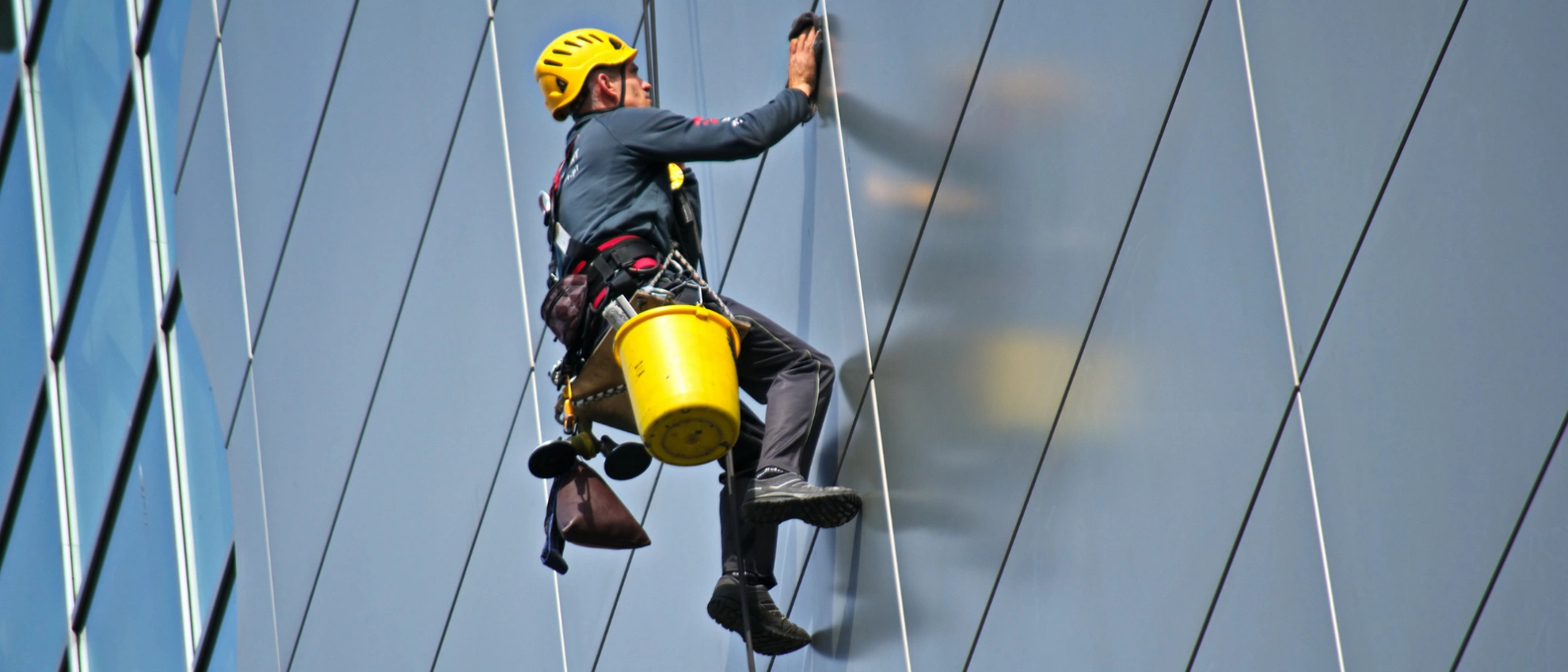 Industriekletterer mit Helm reinigt mit Seilsicherung eine Glasfassade