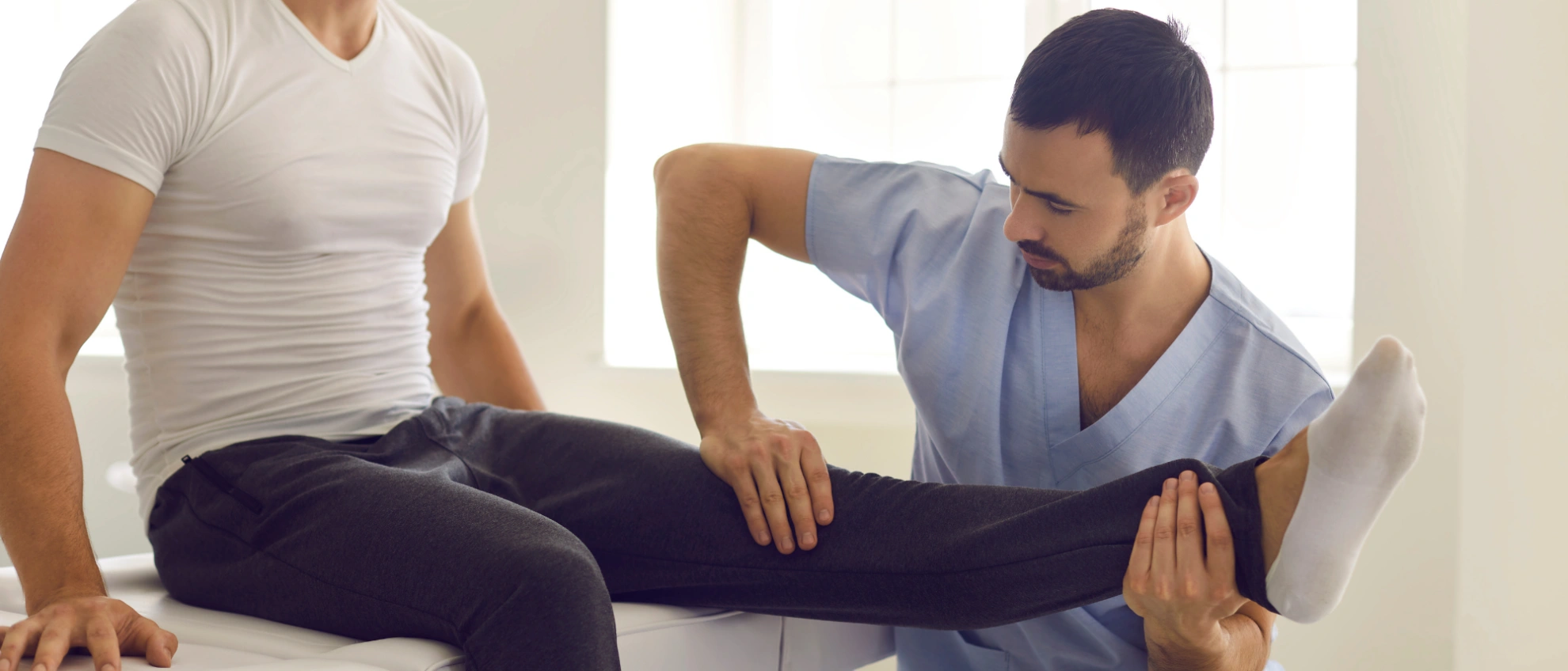 Physiotherapeut dehnt das Bein eines Patienten auf einer Behandlungsliege