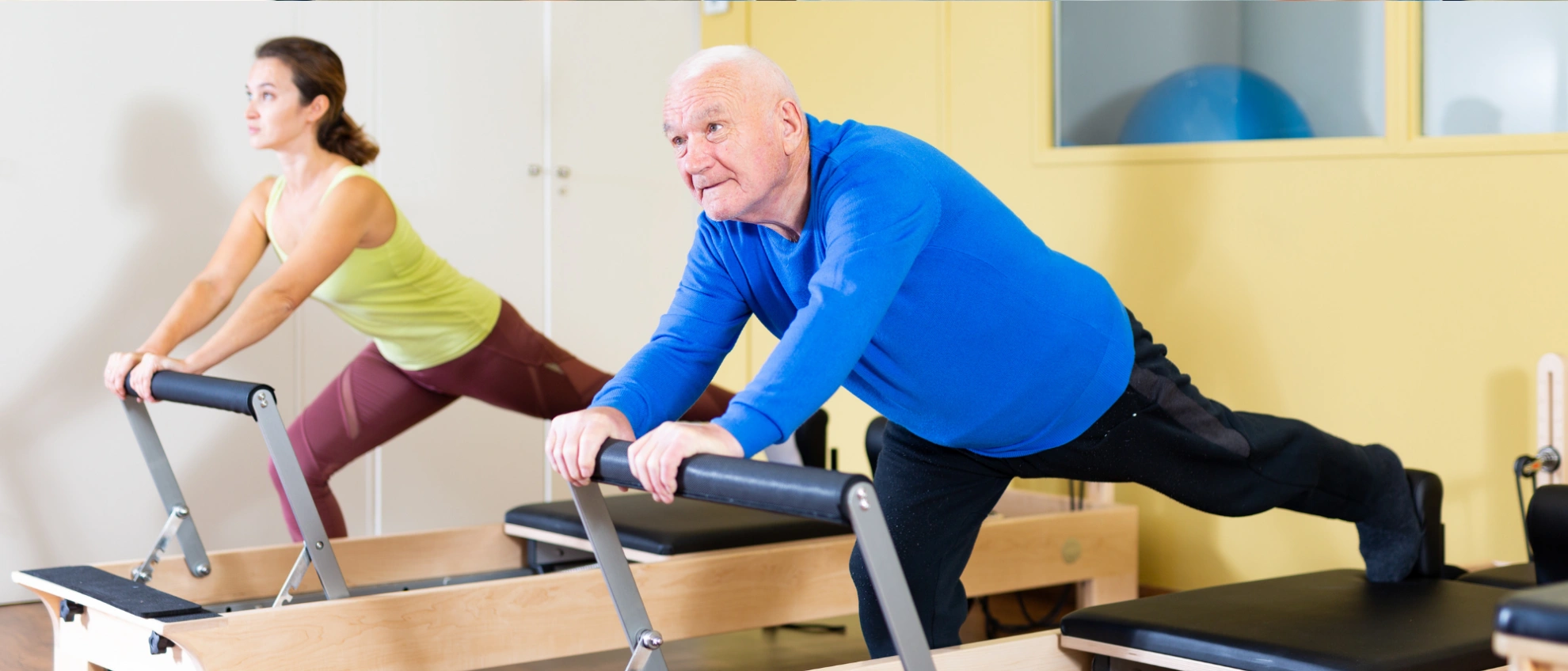 Älterer Mann macht Übungen mit einem Pilatesgerät, im Hintergrund weitere Trainierende
