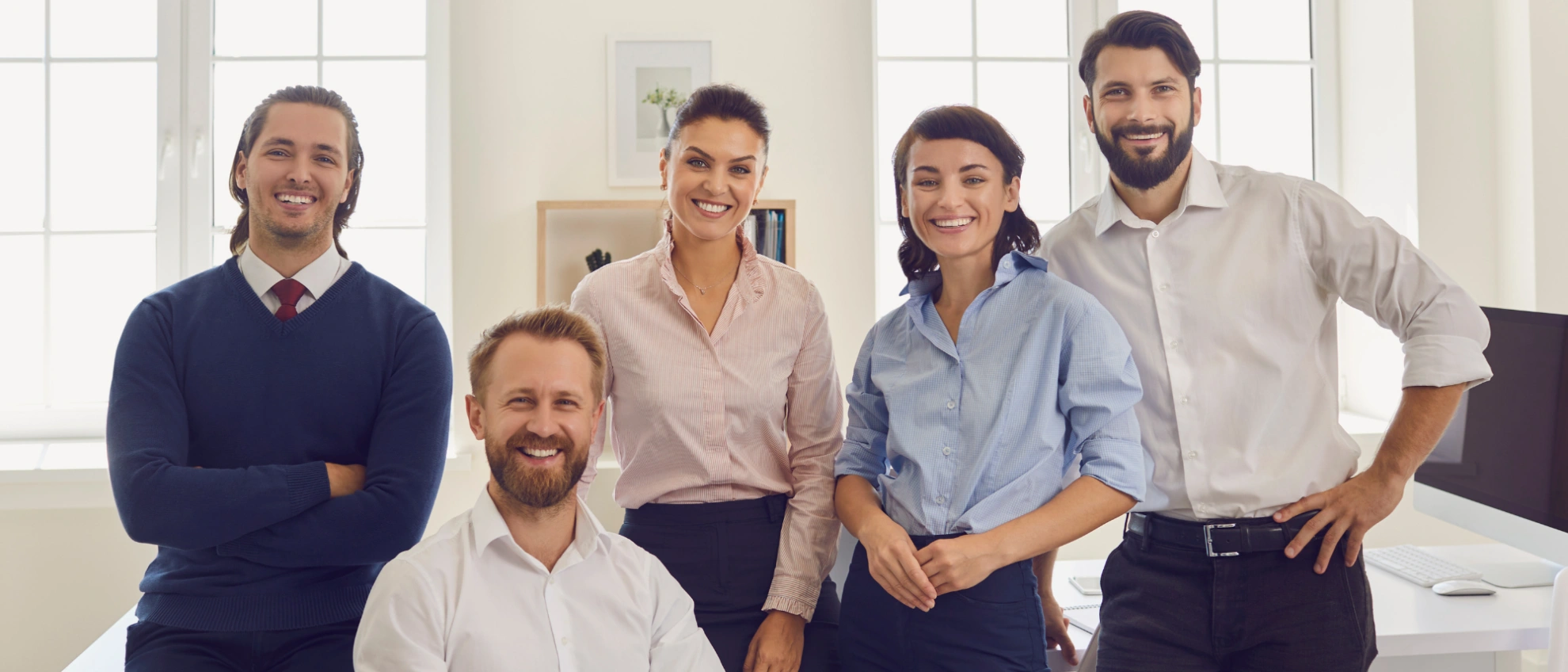 Teamvorstellung einer Personalvermittlung Fünfköpfiges Team steht lächelnd im Büro und blickt in die Kamera