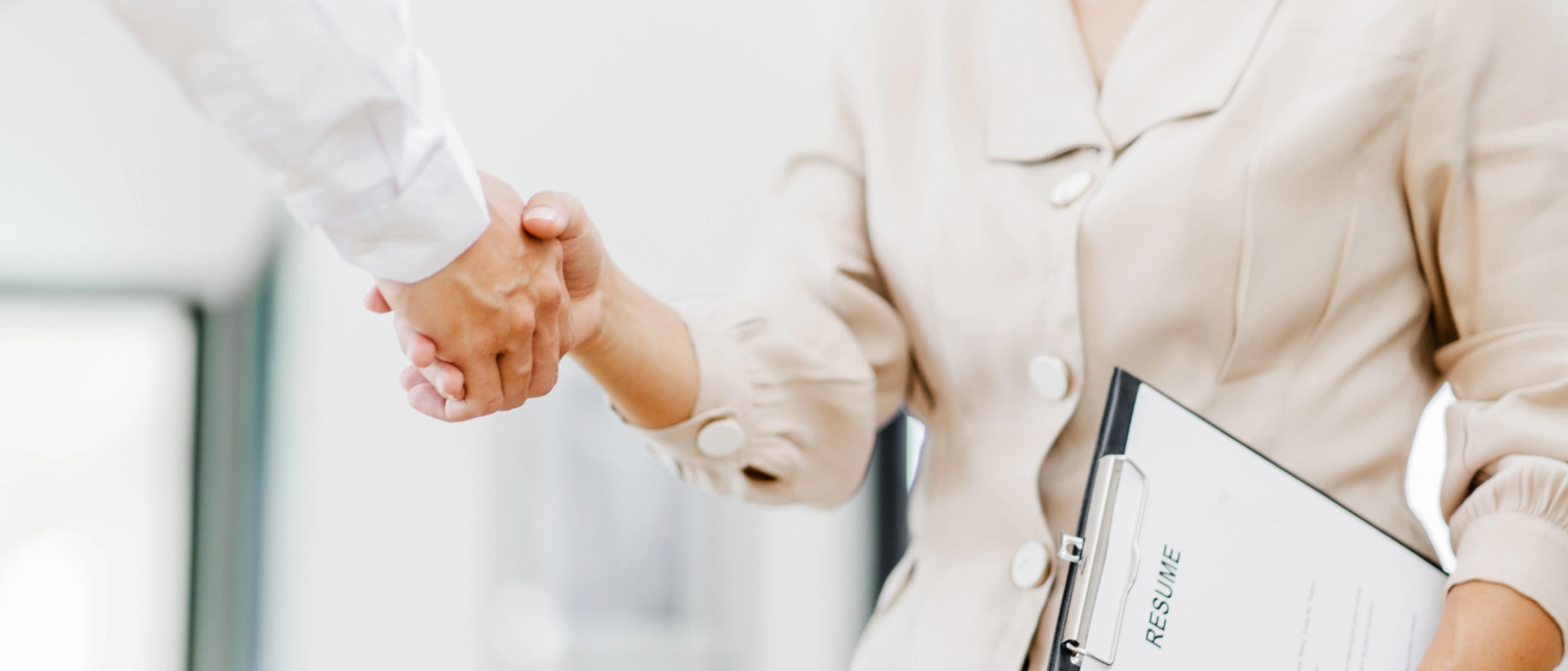 Begrüßung im neuen Job – Handschlag beim Bewerbungsgespräch Zwei Personen geben sich die Hand, eine davon hält eine Bewerbungsmappe